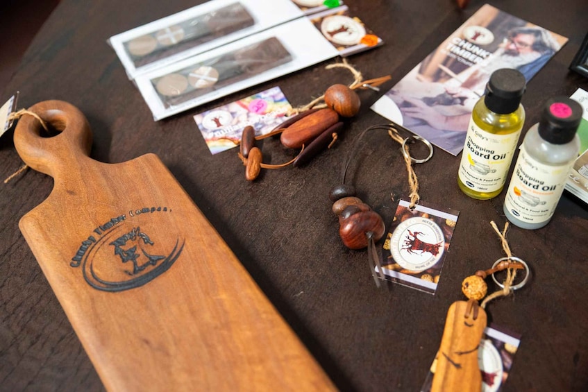 A wooden cutting board with a logo, wooden beads, and two bottles of oil on a table. 4