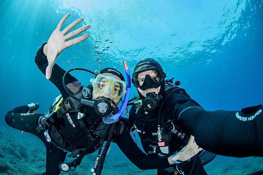 Two scuba divers underwater, one extending a hand towards the camera. 1