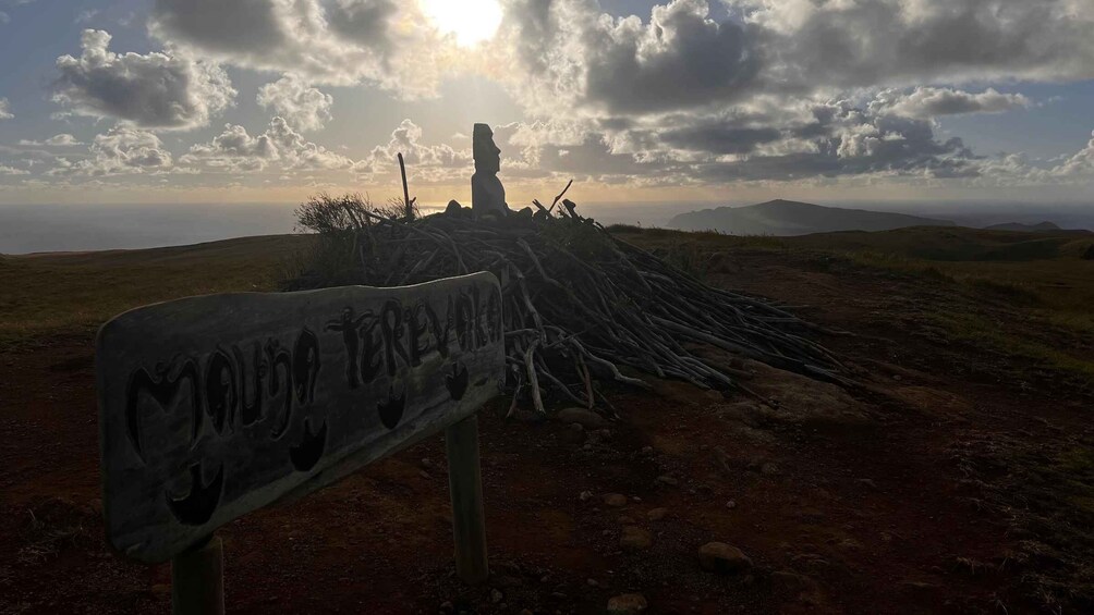 A sign with 'MOUJA TERRE' inscribed, a toppled structure resembling a cross, and a landscape with rolling hills under a partly cloudy sky. 4