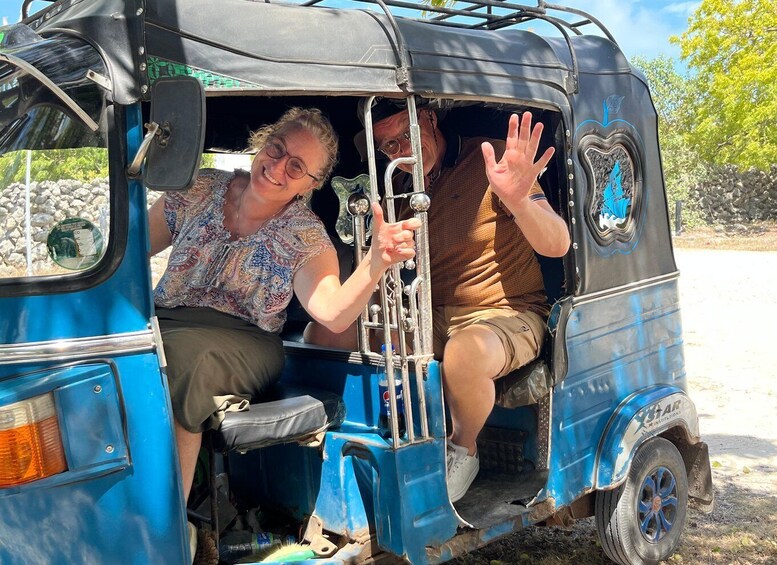 Two people in a blue auto-rickshaw with a decorative emblem on the side. 2