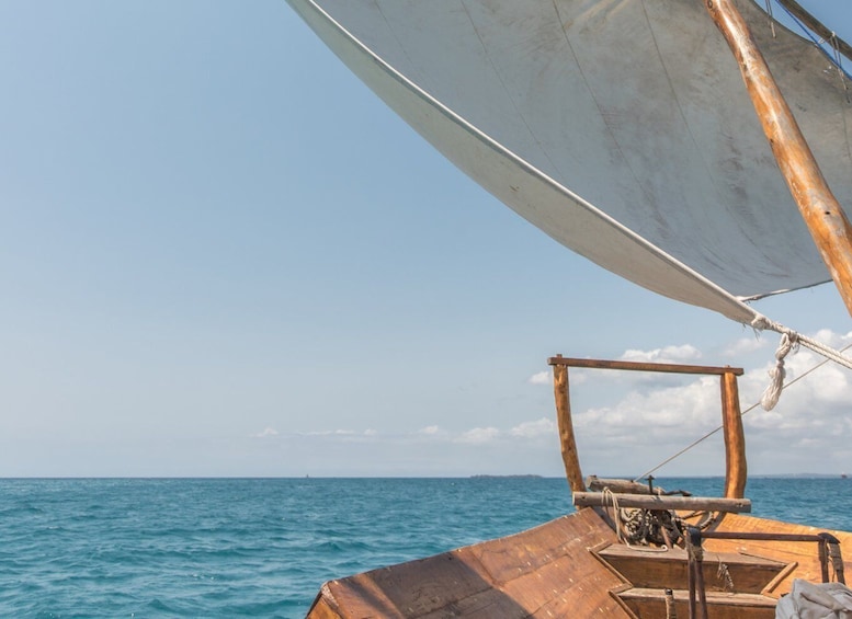 A wooden boat with a white sail on the ocean. 1