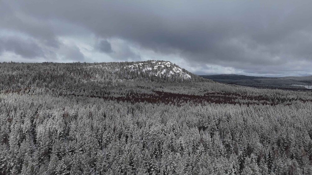 A forested mountain with snow-capped peaks under a cloudy sky. 3