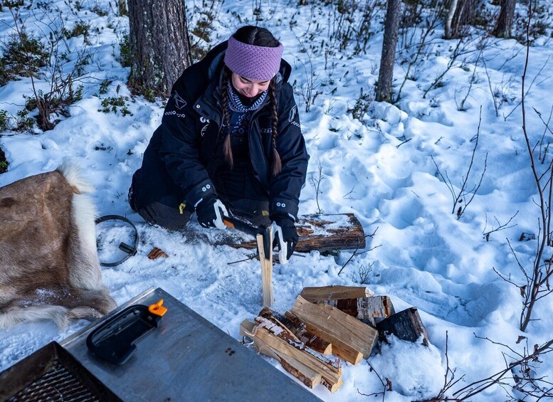 A person in a snowy forest setting, preparing firewood for a campfire. 2