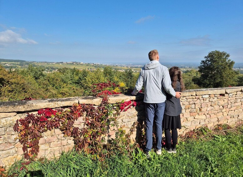 Two people standing on a stone wall overlooking a landscape with greenery and a distant view of a town. 2