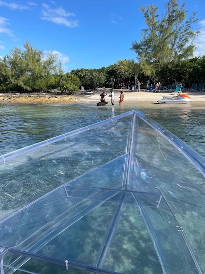 A transparent boat on clear water with a beach and people in the background. 1