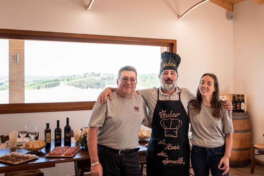 Three people standing in a room with a table of food and wine. 5