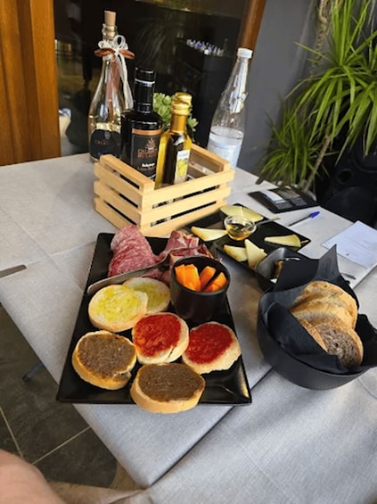 A charcuterie board with various meats, cheeses, and breads, accompanied by bottles of wine and olive oil. 3