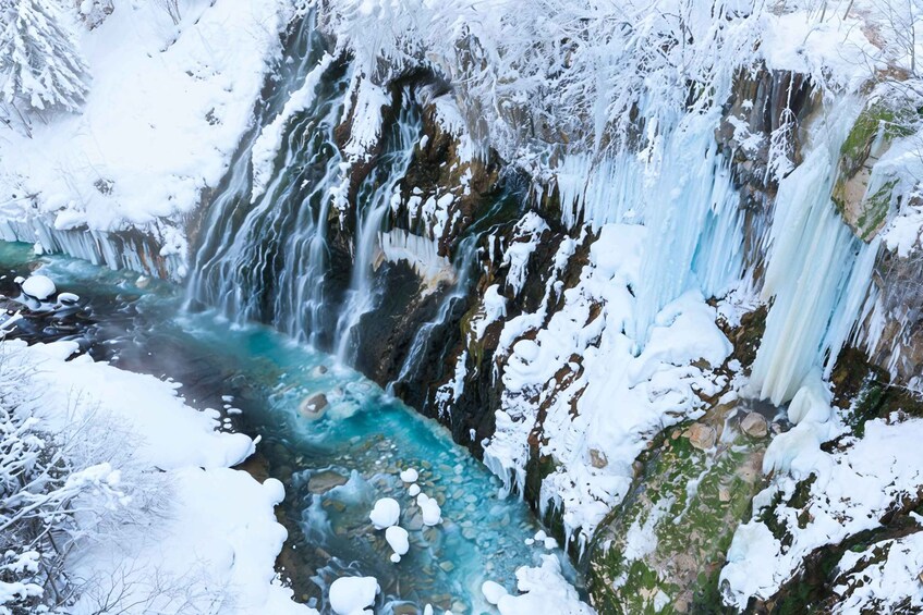 A frozen waterfall with clear water flowing through it, surrounded by snow-covered rocks and trees. 3