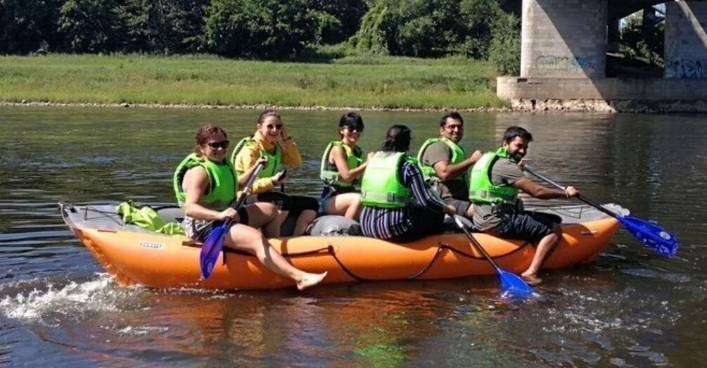 A group of people in an orange raft on a river, wearing life jackets. 1