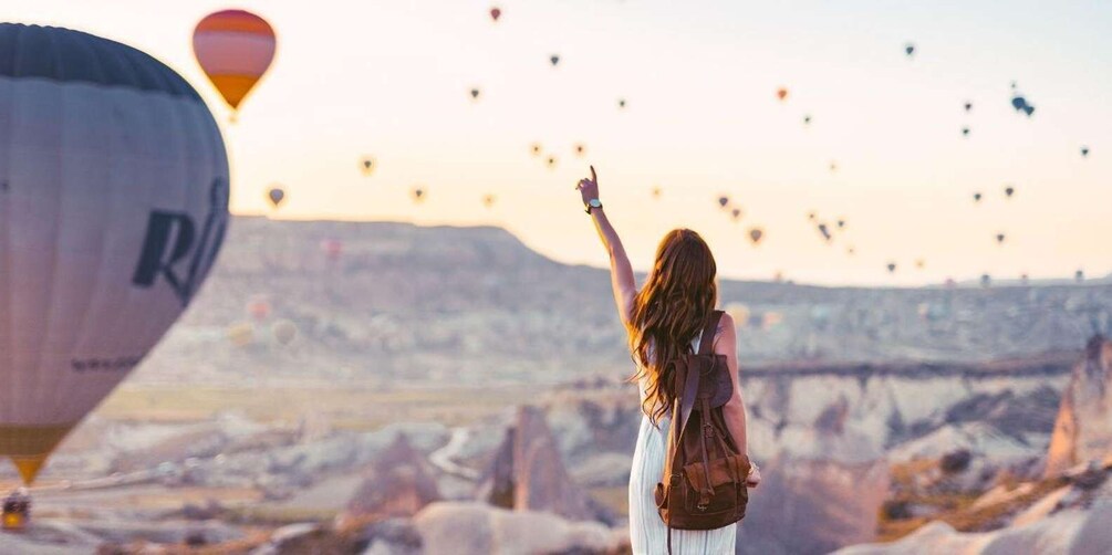 A person with a backpack looking at hot air balloons in the sky. 5