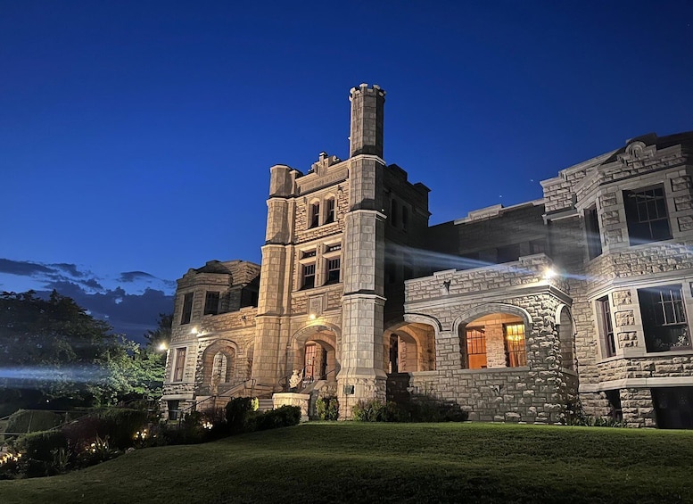 A large, historic stone building with arched windows and a prominent tower, illuminated at dusk. 3