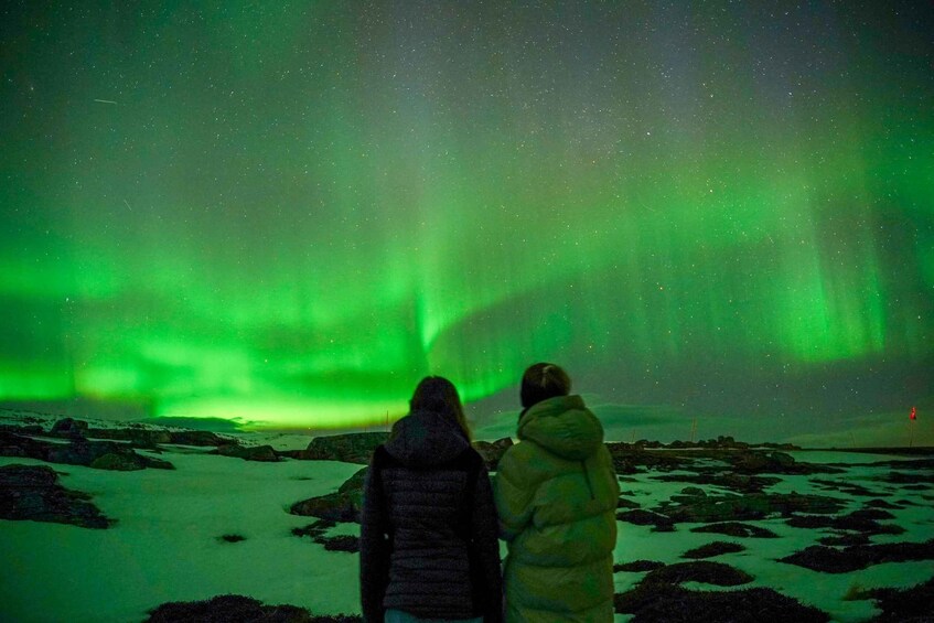 Two people observing the Northern Lights over a snowy landscape. 4