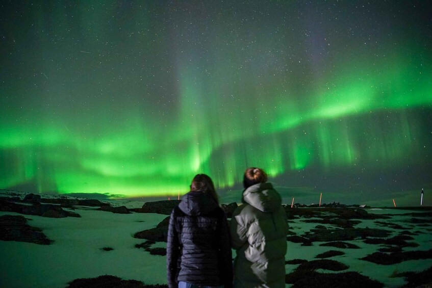 Two people observing the Northern Lights over a snowy landscape. 2