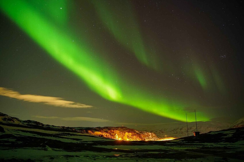 The Northern Lights over a snowy landscape with a lit building. 3