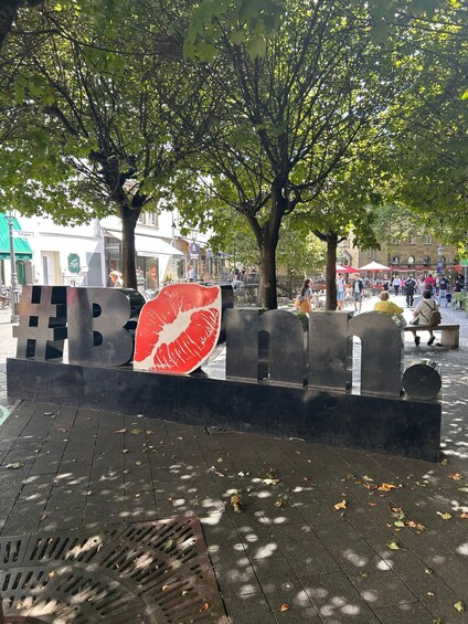 A public square with a large red lips sculpture, trees, and a paved walkway. 4