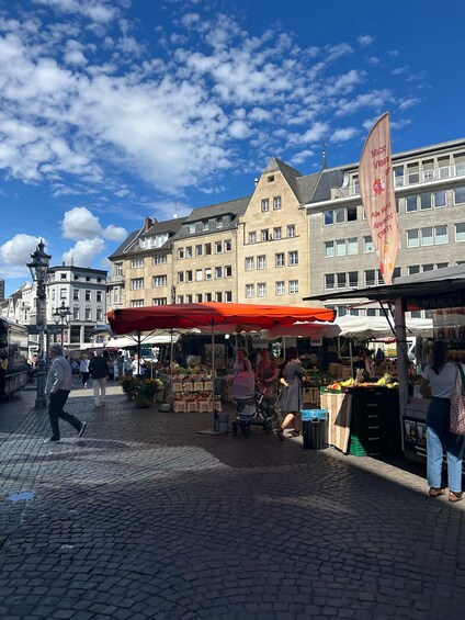 A cobblestone street with market stalls, pedestrians, and historic buildings under a partly cloudy sky. 2