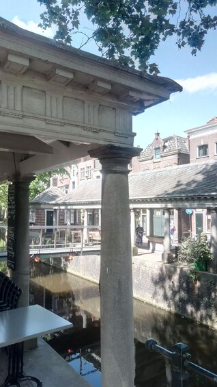 A covered outdoor area with a canal, brick buildings, and a table with chairs. 5