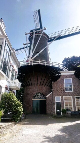 A traditional windmill with a brick base and a metal lattice structure, surrounded by buildings. 4