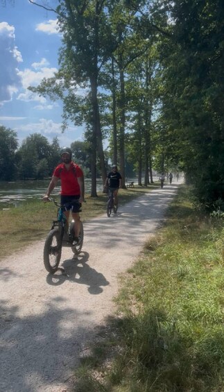 A gravel path with cyclists, surrounded by trees and a body of water. 2