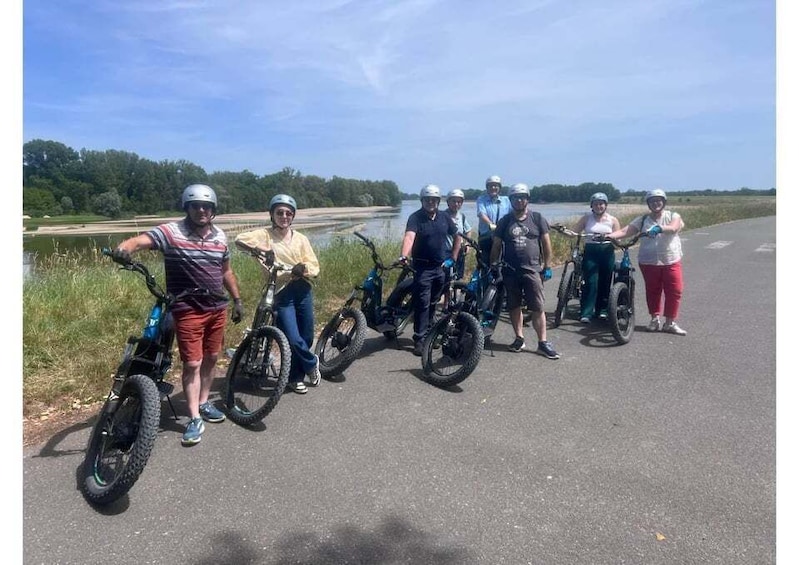 A group of people with bicycles on a paved road near a body of water. 5