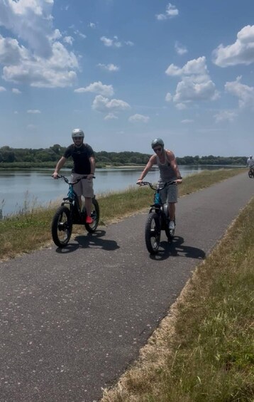 Two people riding electric bikes on a paved path by a lake. 3