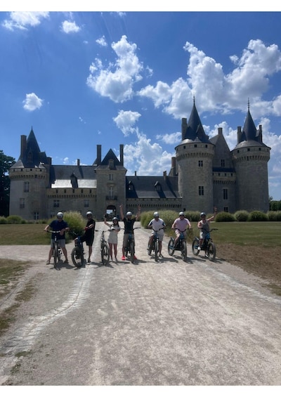 A group of cyclists on a dirt path in front of a castle. 1