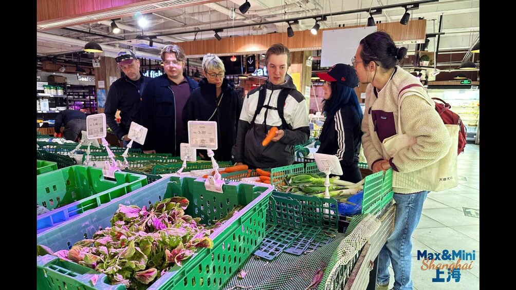 A group of people shopping at a produce section in a supermarket with green crates of vegetables. 2