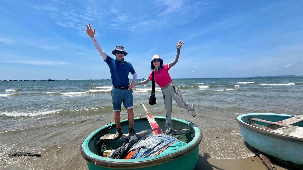 Two people standing in a boat on a beach with the ocean in the background. 1