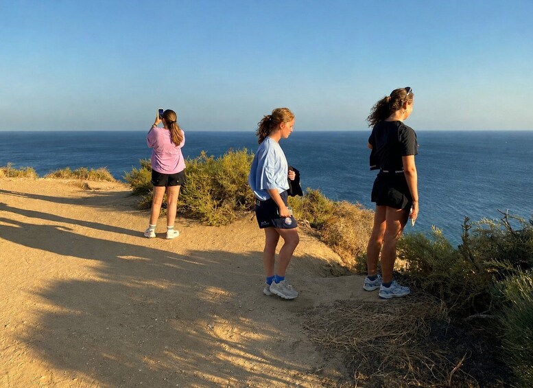 Three people standing on a dirt path overlooking the ocean. 4