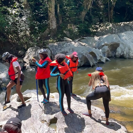 A group of people in red life vests standing on rocks by a river. 3