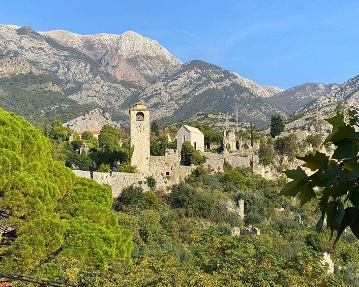 A historic stone church with a bell tower, surrounded by lush greenery and mountains. 3