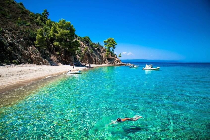 A clear turquoise sea, a sandy beach, and a rocky cliff with trees. 1
