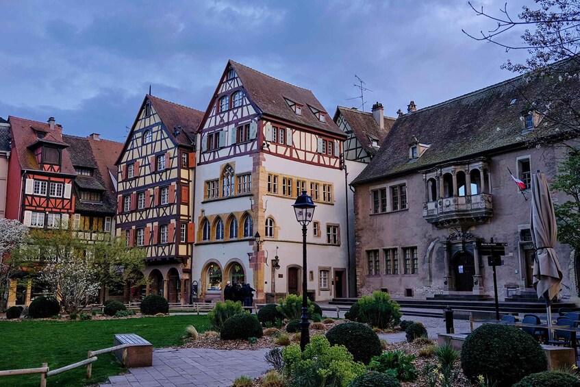 A historic European town square with traditional half-timbered buildings and a well-maintained garden. 1