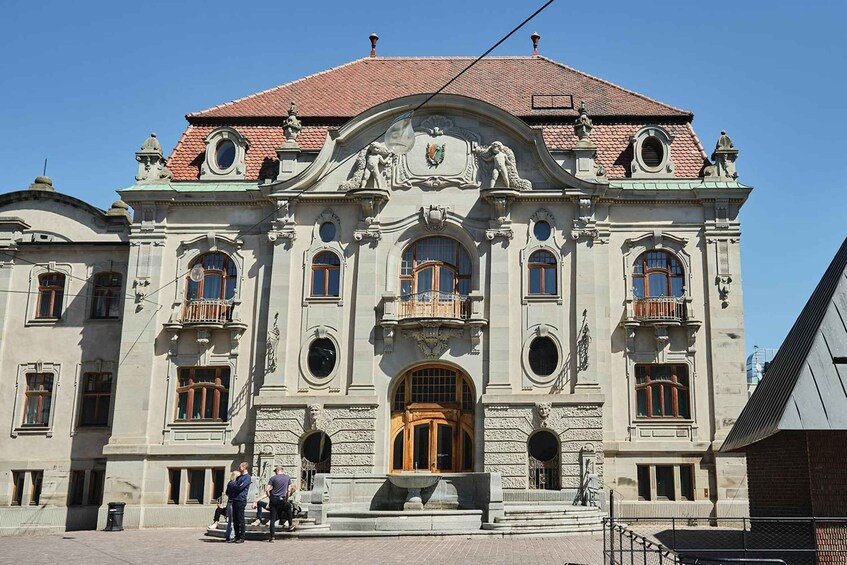A historic building with ornate architecture, including a central entrance with a wooden door, decorative balconies, and a red-tiled roof. 4
