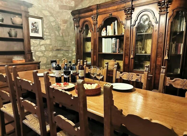 A wooden dining table with chairs, wine bottles, glasses, and a basket of bread. 5