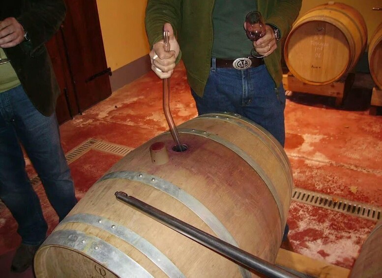 A wooden barrel with metal hoops and a long metal rod inserted into it, held by a person. 3