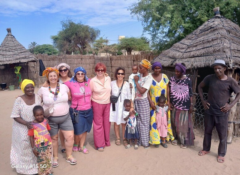 A group of people standing in front of thatched-roof huts in a rural setting. 3