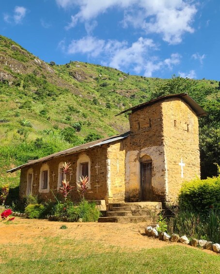 A small stone church with a bell tower, surrounded by greenery and a hillside. 3