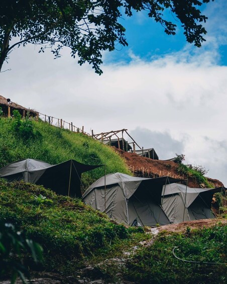 A campsite with tents on a grassy hill, a wooden structure, and a clear sky. 1