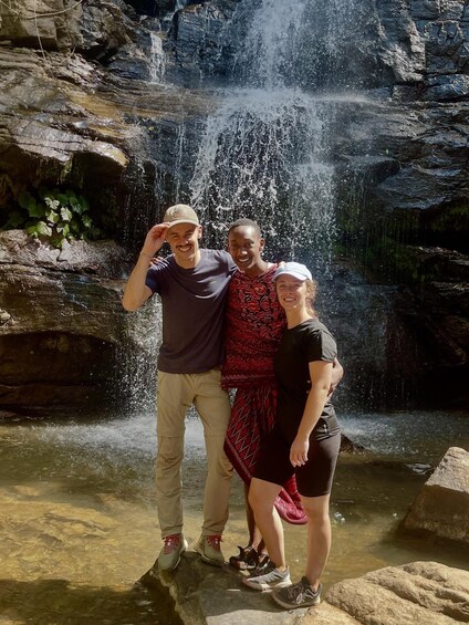 Three people standing in front of a waterfall with water cascading down a rocky cliff. 2