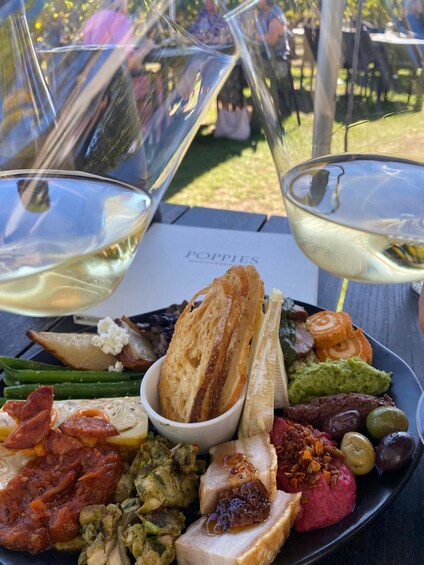 A charcuterie board with various cheeses, meats, and olives, accompanied by two glasses of white wine. 2