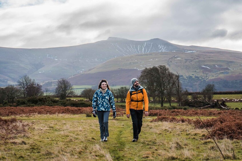 Two people walking on a grassy field with a mountain in the background. 1
