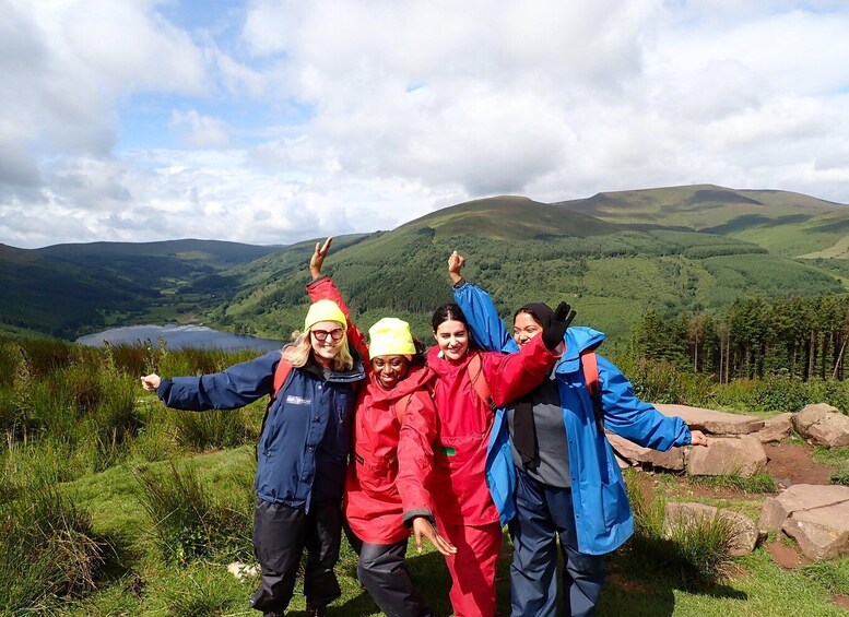 Four people in outdoor gear posing on a grassy hill with a lake and mountains in the background. 2