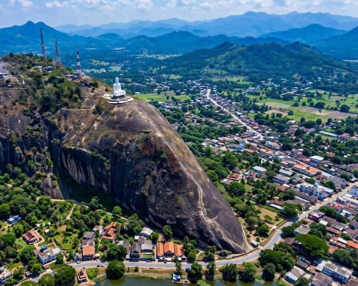 A large rock formation with a white structure on top, a town below, and mountains in the background. 2