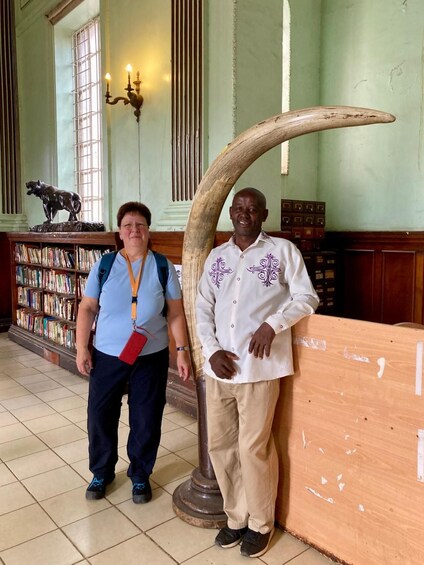 Two people standing in a library with bookshelves and a large tusk sculpture. 5
