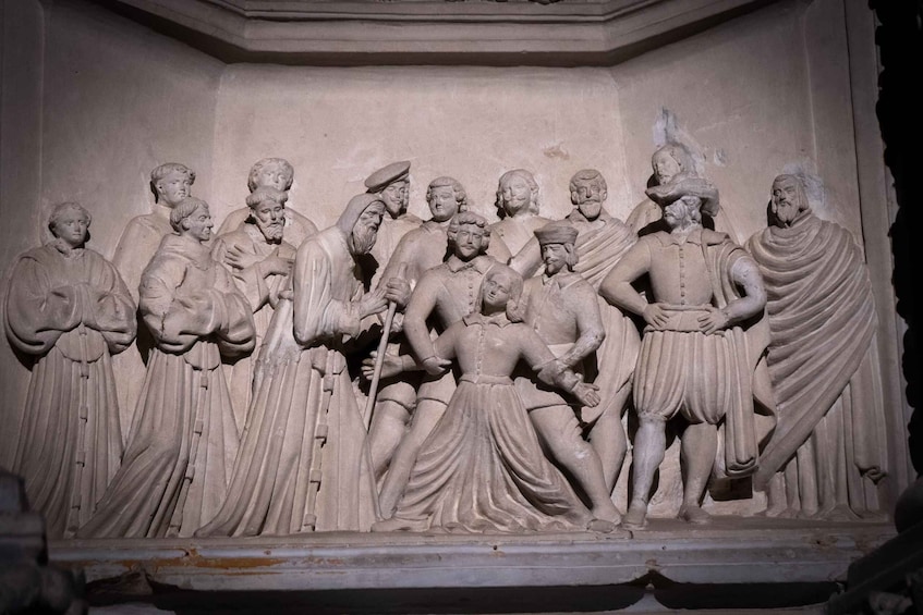 A detailed stone relief sculpture depicting a group of historical figures in classical attire, with one figure holding a staff and another in a dynamic pose. 5