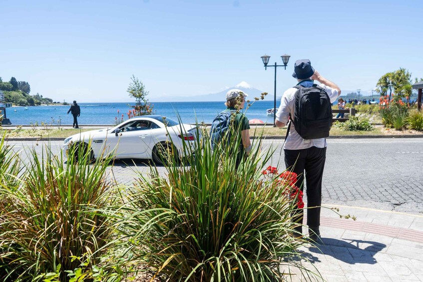 A coastal road with a white car, a person with a backpack, and a mountain in the background. 5
