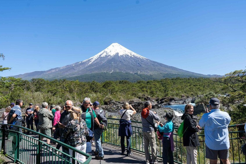 A group of people standing on a bridge, overlooking a snow-capped mountain. 1