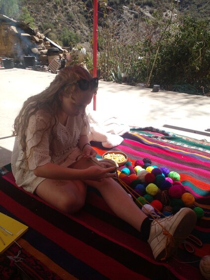 A person sitting on a colorful blanket, knitting with yarn and knitting needles. 4