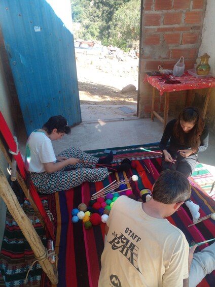 A group of people engaged in crafting activities, with colorful yarn and knitting needles on a mat. 3